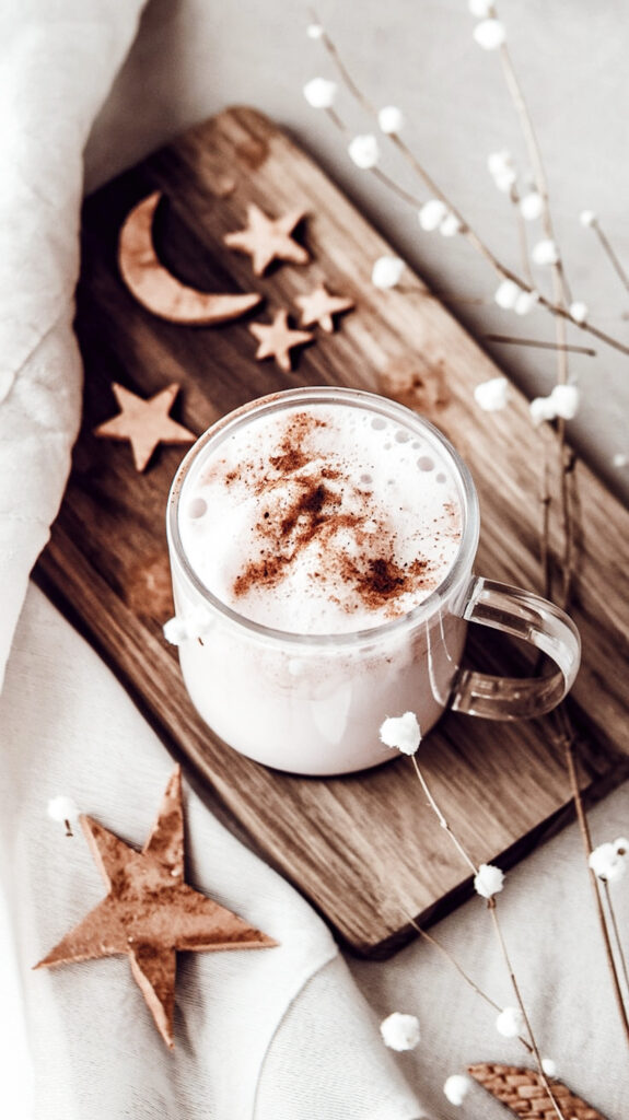 Adaptogenic moon milk for better sleep in a cozy glass mug, topped with frothy foam and dusted with cinnamon.